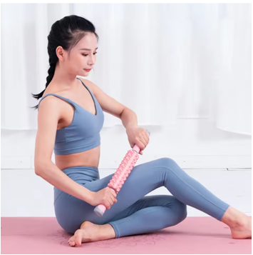 femme sur tapis massant cuisse avec rouleau de massage rose
